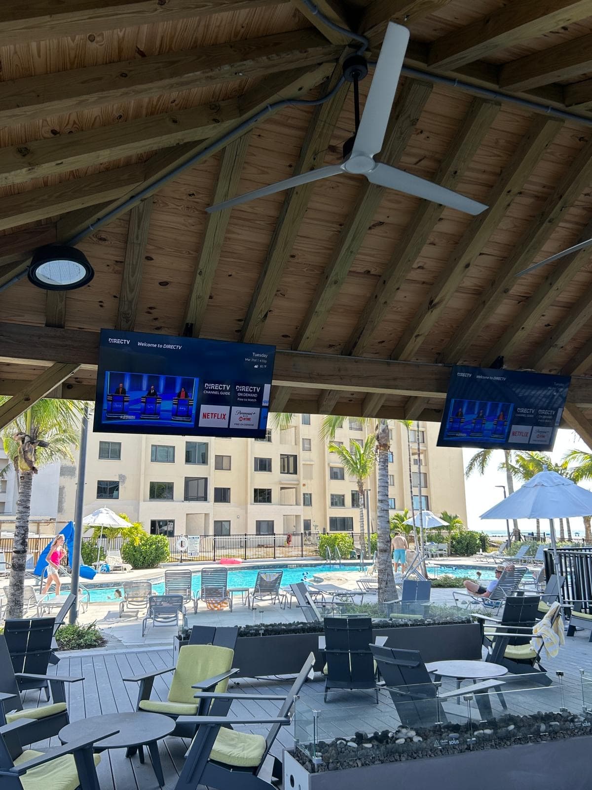 Pool deck pavilion with overhead-mounted DIRECTV displays and ceiling fans