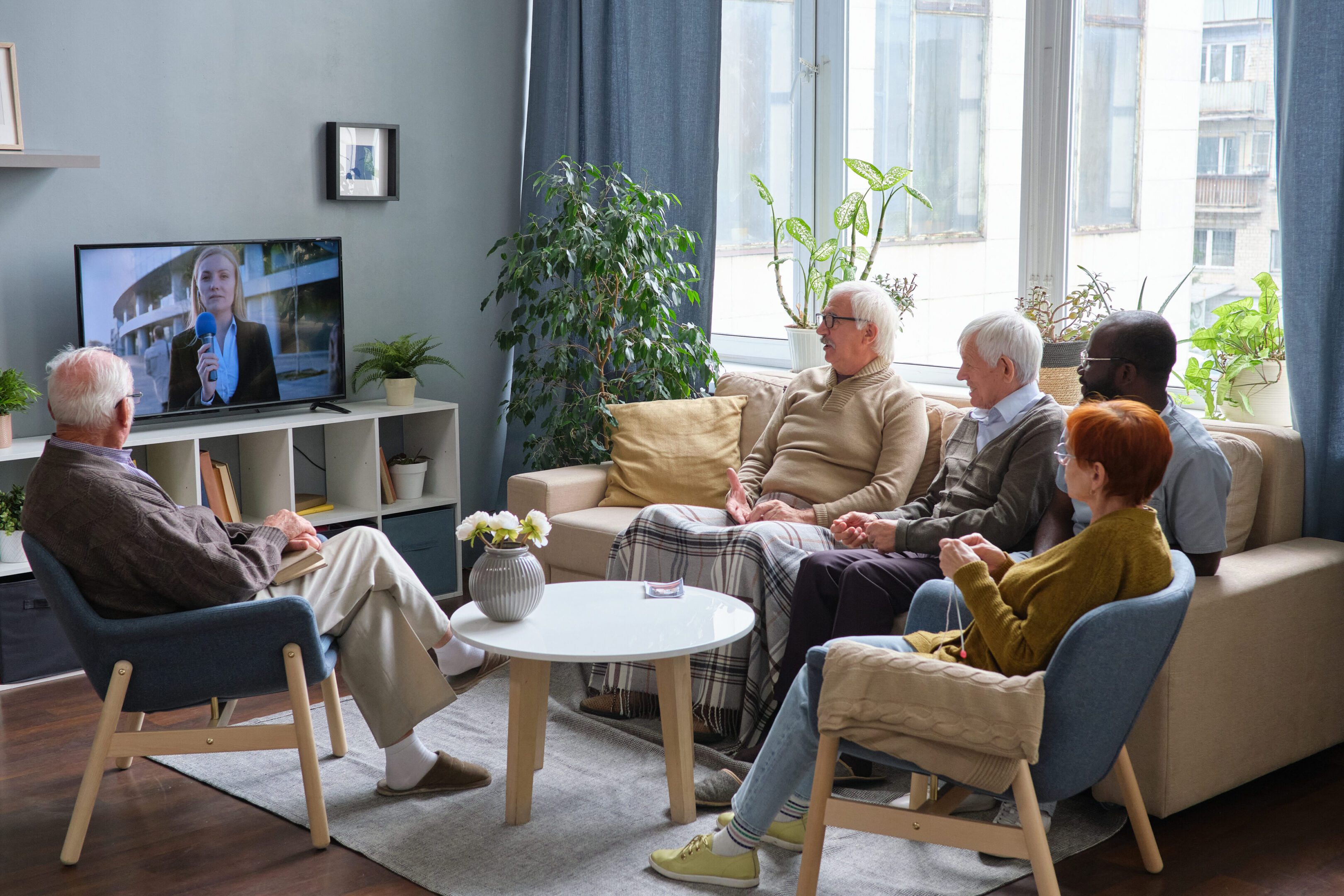 Elderly people chatting in a cozy living room with plants and natural light.