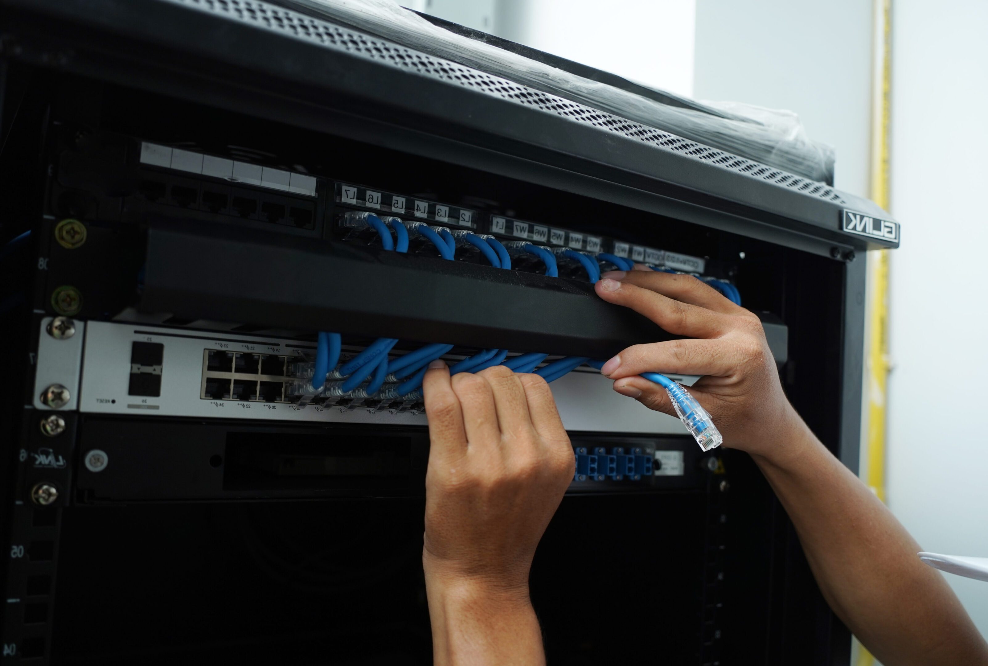 Hands organizing blue Ethernet cables in a network switch panel.