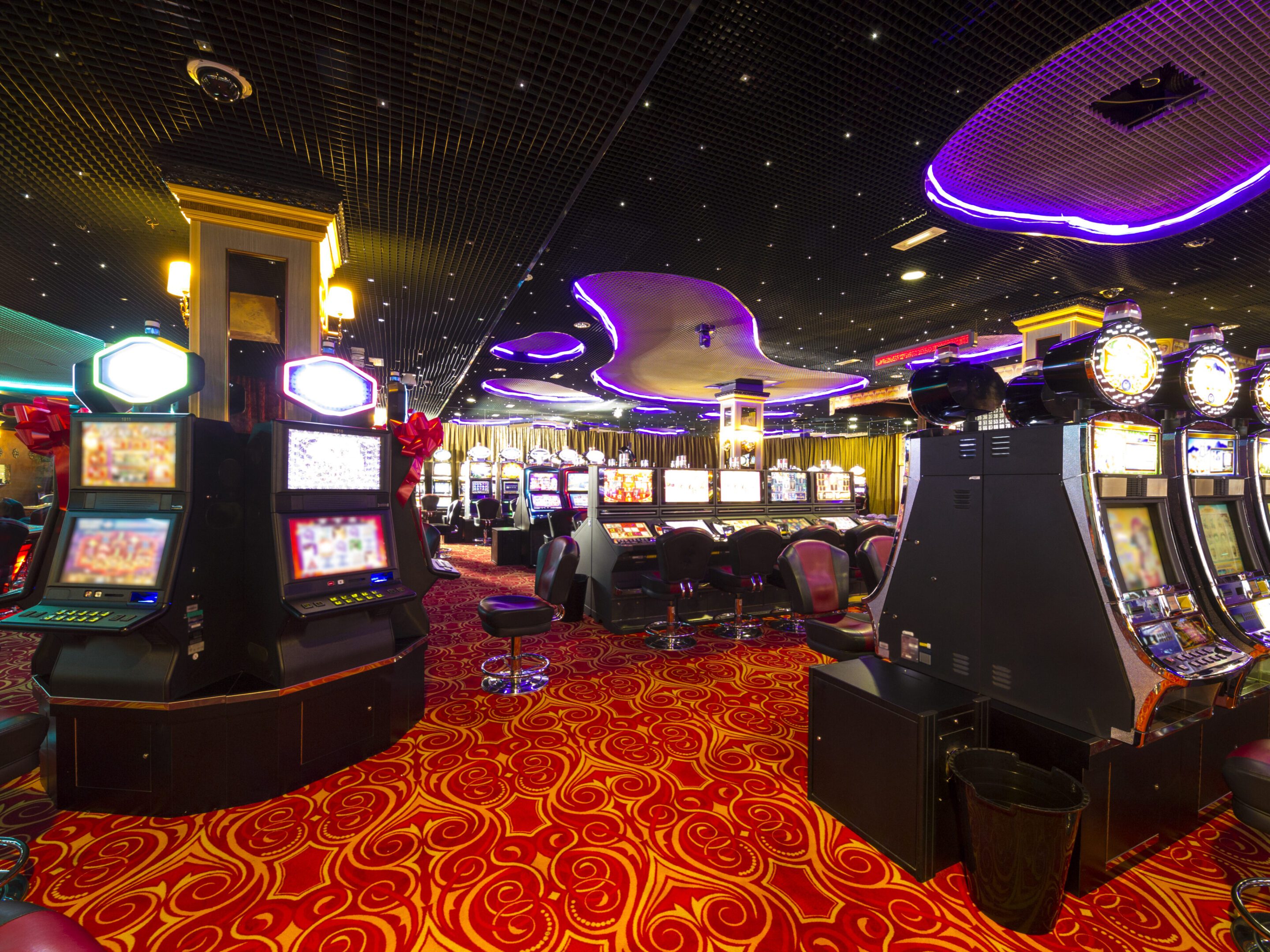 Brightly lit casino floor with slot machines and vibrant red carpet.